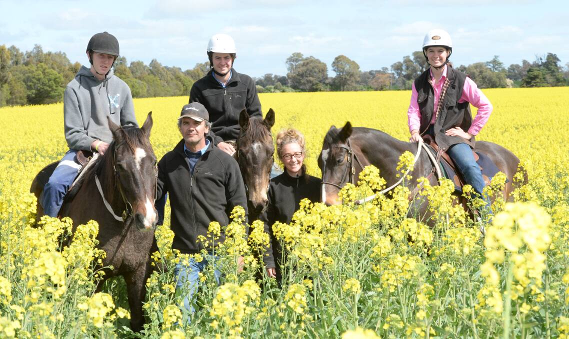 Angus Metcalfe and Alex Dalglish (standing), 'Olde Milong', Young, and (on horseback) Lachie Doust, 15, Will Metcalfe, 15, and Tilly Metcalfe, 13, in a paddock of canola bordered by trees direct seeded and planted in 2002. 