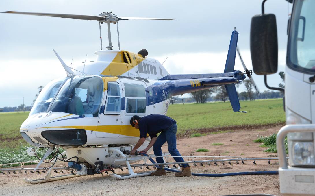 Commercial Helicopters pilot Sam Nichols, Mudgee, sits in the cockpit while James Brown, Mudgee, refills the chemical at "West Wai", Trangie.