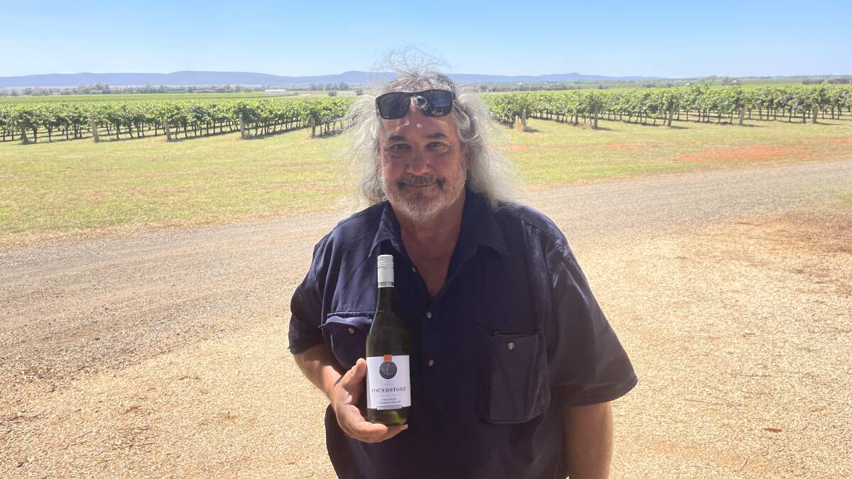 Bob Berton proudly displaying a bottle of Chardonnay from the vines behind him.