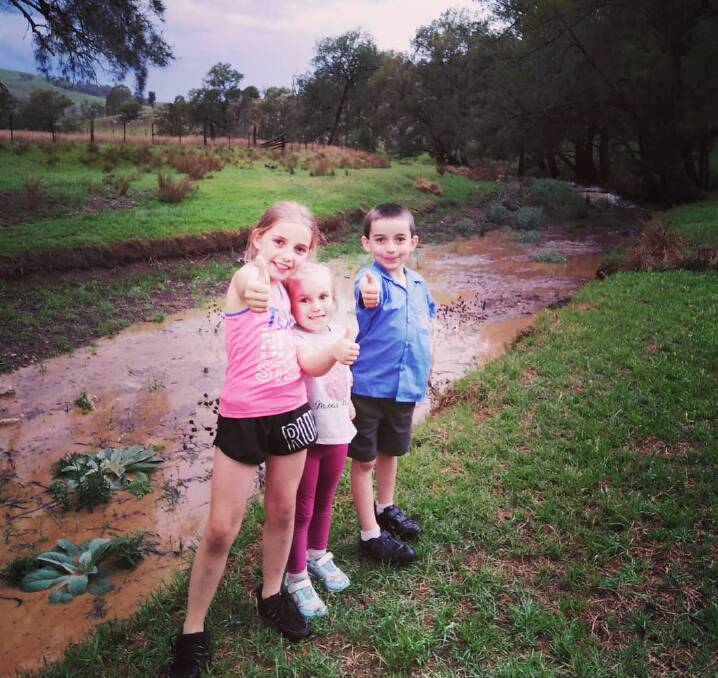 Chyann Brown with her siblings Elliyah and Tyler at their Hunter Valley property where a downpour has seen the creek that runs through their property flow for the first time in 1.5 years. Photo by Julie Brown.