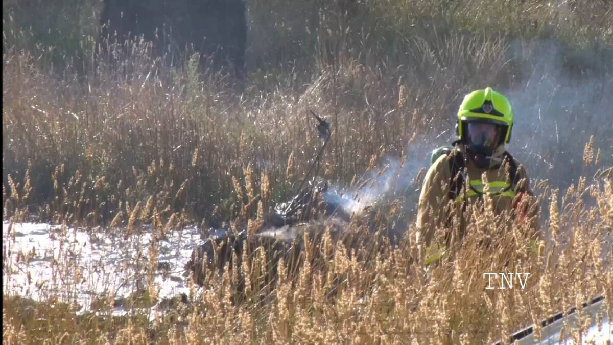 CRASH: Fire crews with the smouldering wreckage of the helicopter after it crashed south of Orange on Saturday. Photo: TROY PEARSON/TNV