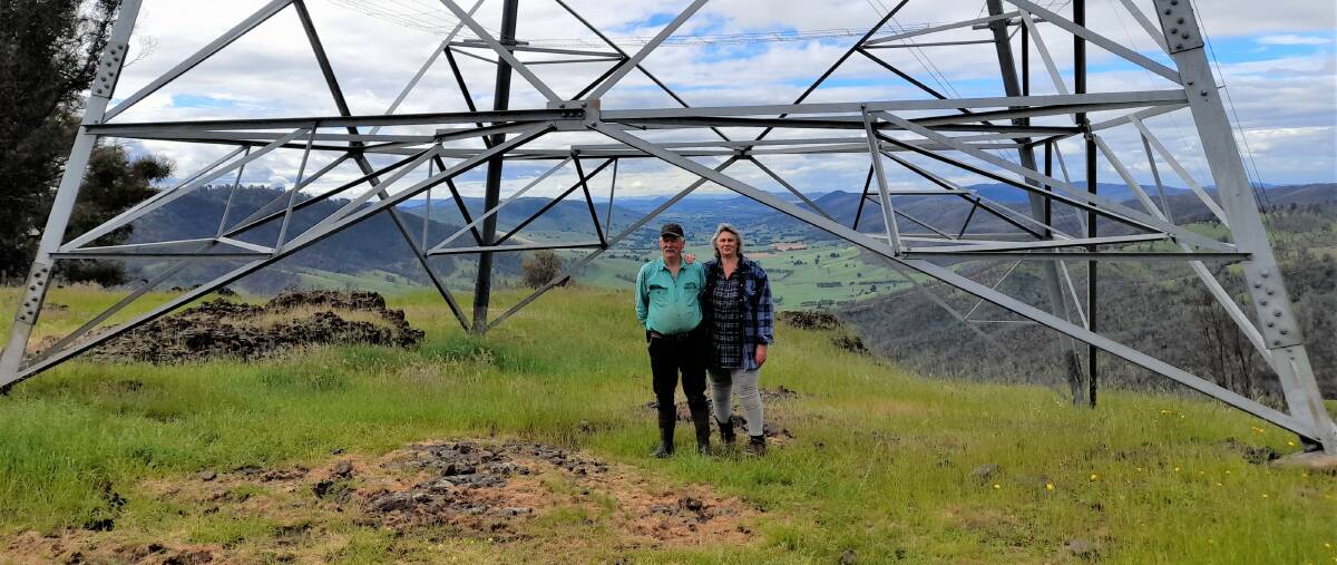 Paul and Andrea Sturgess at Batlow stand under the existing 330kv Yass 03 power line tower on their property. The new 500kv towers TransGrid want to build are 75m tall, double the height of current ones.